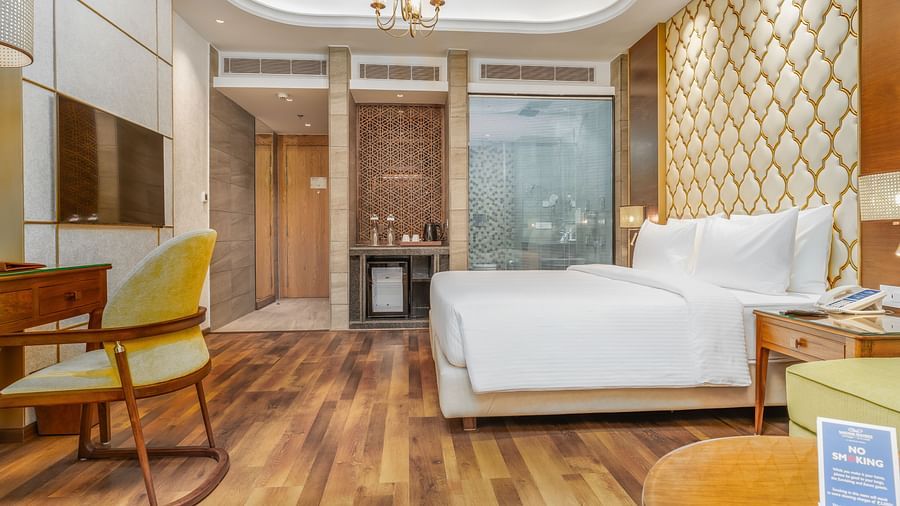 An image of a room with a chandelier, a double bed, a writing desk and a wall-mounted television - Sarovar Premiere, Srinagar 